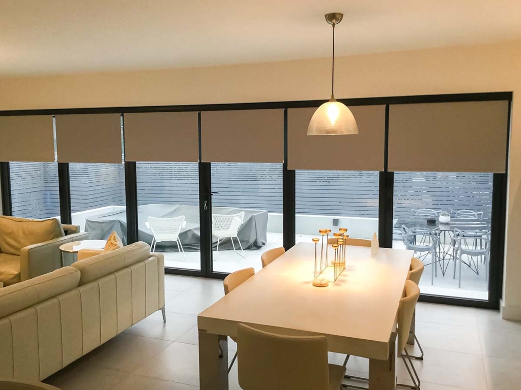 Multiple roller blinds fitted in front of folding doors.