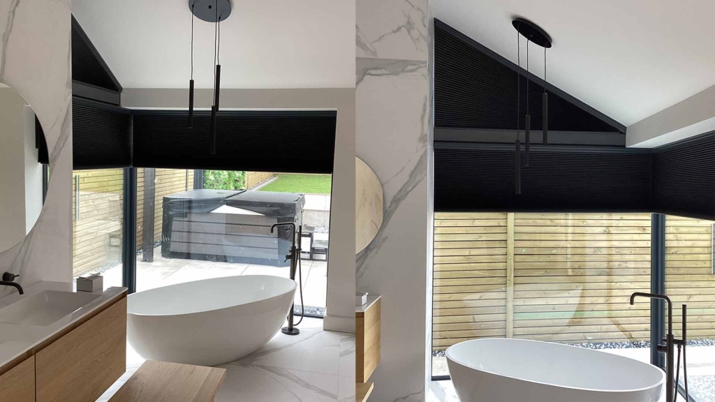 Black blinds in a modern bathroom with a free standing bath and corner window